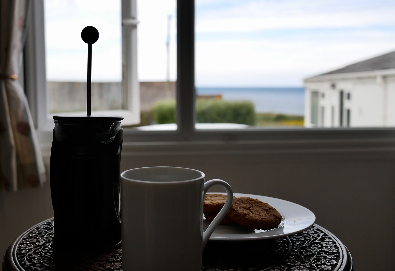 Café e vista para o mar de dentro de uma casa de campo.