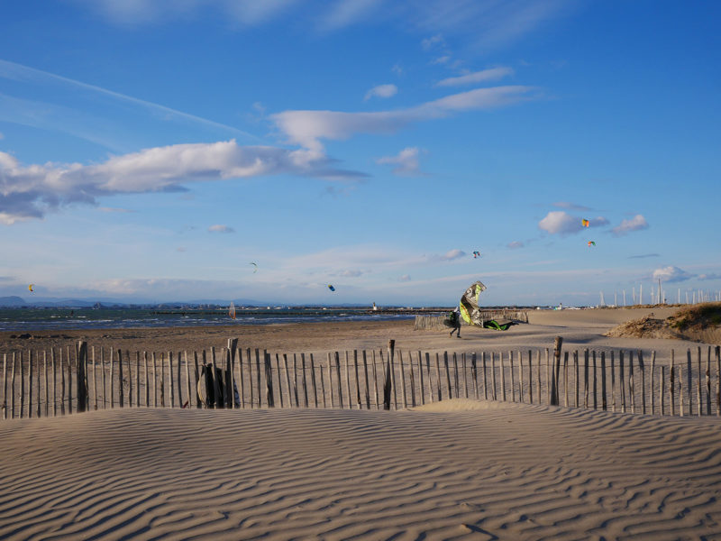 En vakker strand og en kitesurfer som bærer dragen sin etter en økt.