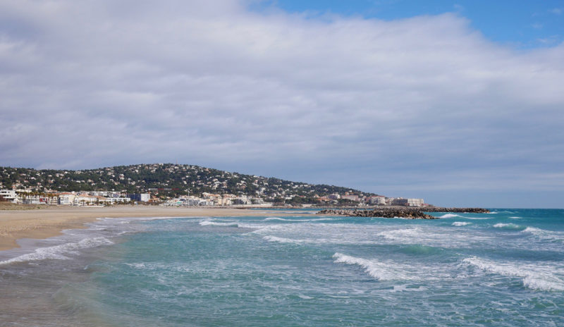 A wild and empty beach with Sete in the background.