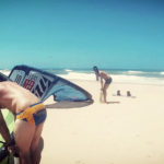 två manliga kitesurfer som dumpar drakar på stranden i skimpy badkläder.